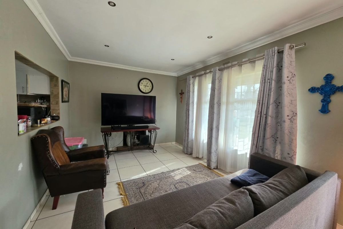 A comfortable living room featuring tiled flooring, recessed downlighting, and a convenient pass-through window connecting to the kitchen area.