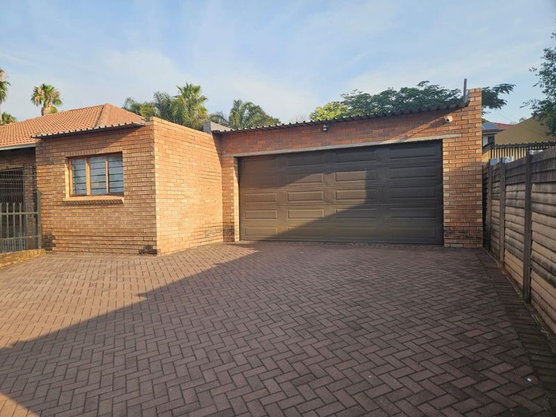 Exterior view of a brick-built garage with a sectional door and a paved driveway, featuring a secure boundary wall and exterior lighting.