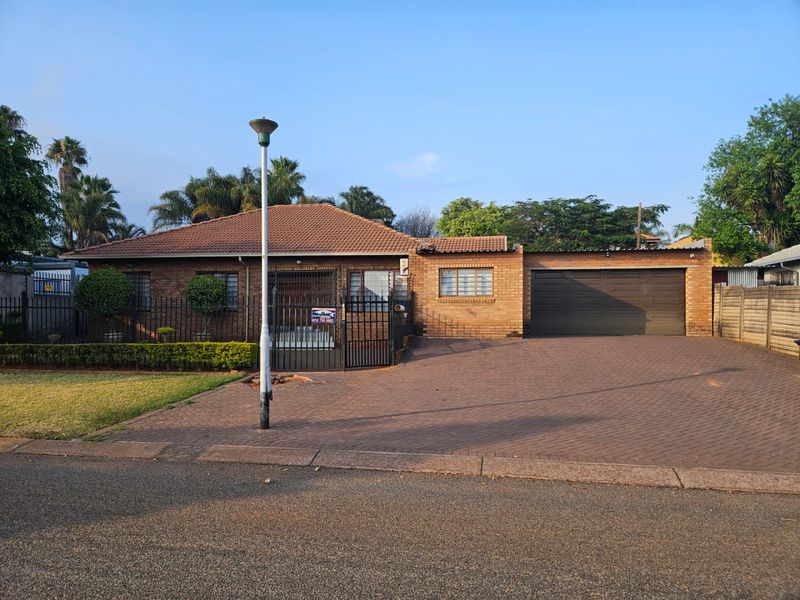 A well-maintained single-story brick house featuring a tiled roof, paved driveway, and an integrated double garage with secure perimeter fencing.