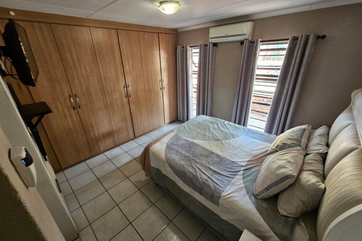 A functional bedroom featuring built-in wooden cupboards, tiled flooring, and a wall-mounted air conditioning unit.