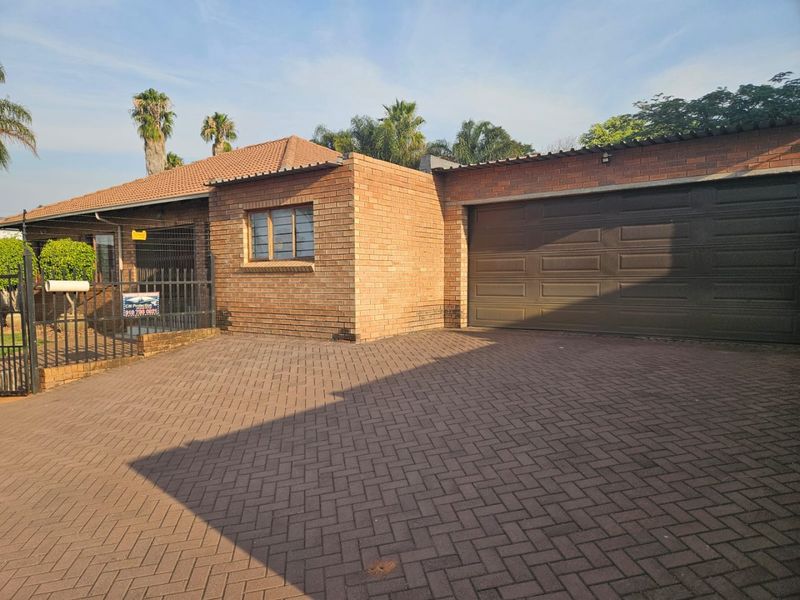 Front exterior view of a brick house featuring a paved driveway, secure metal gate, and an integrated garage.