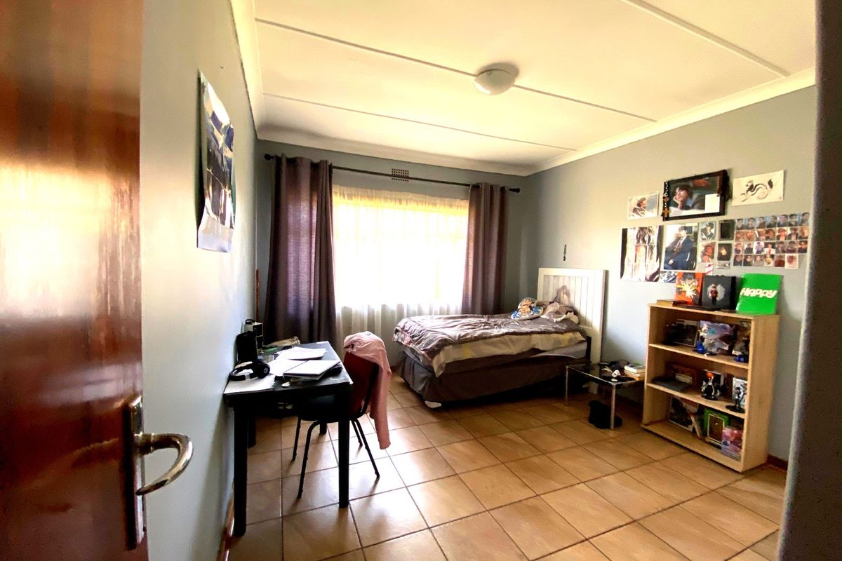 A functional bedroom featuring tiled flooring, neutral wall paint, and a large window with curtain rod, providing a comfortable living space.