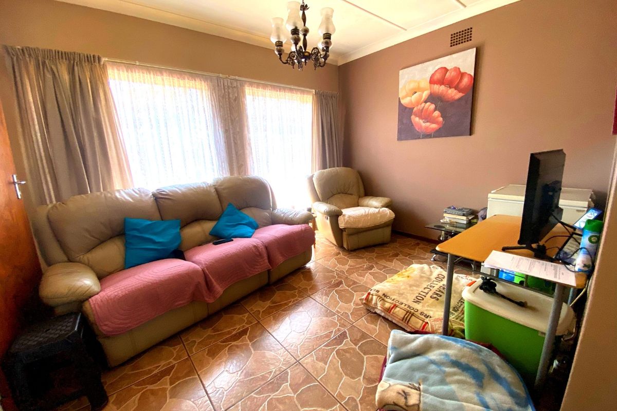 A living room featuring tiled flooring, a central chandelier, and large windows with curtains, providing a functional and lived-in space.