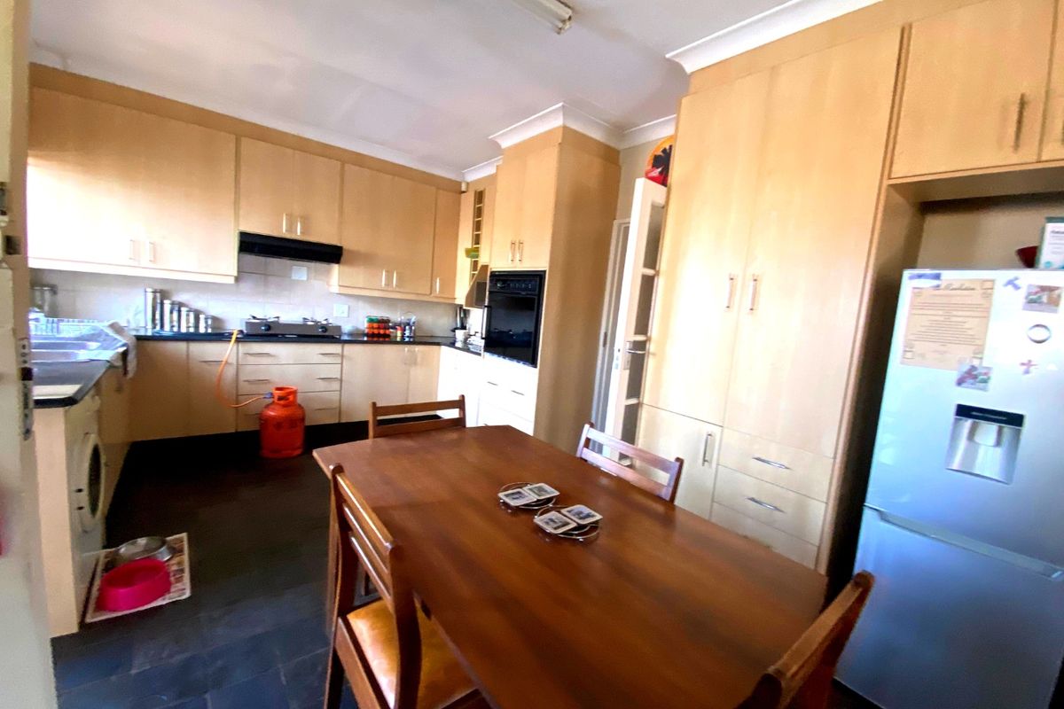 A functional kitchen featuring light wood cabinetry, built-in oven, extractor fan, and dark tiled flooring, offering ample storage and workspace.