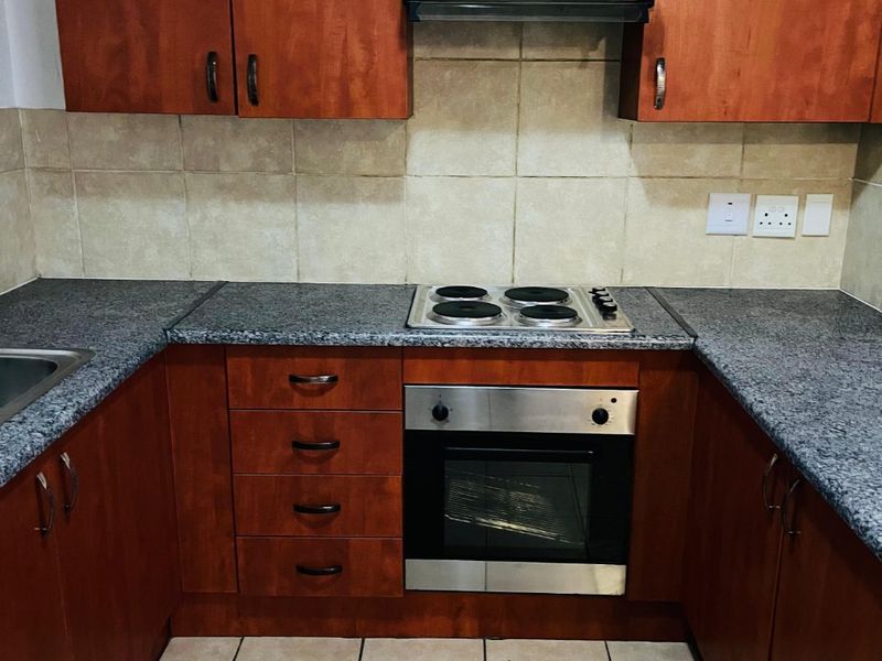 A functional U-shaped kitchen featuring wood-finish cabinetry, granite countertops, built-in oven, electric hob, and tiled backsplash.