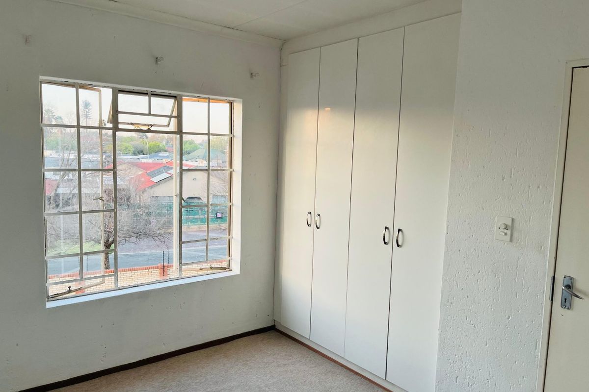 An empty bedroom featuring built-in cupboards, carpeted flooring, and a steel-framed window with a view of the surrounding neighborhood.