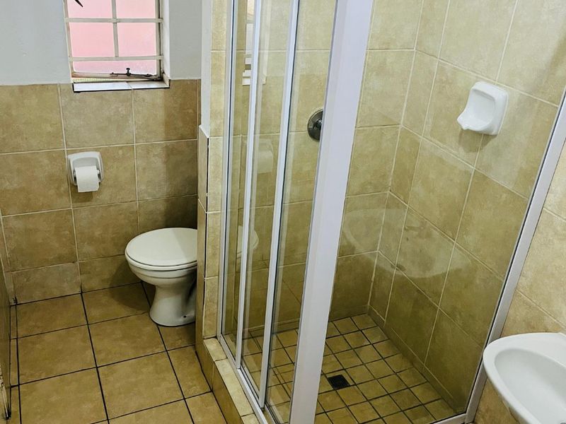 A functional bathroom featuring a shower enclosure, pedestal basin, and toilet with neutral tiled finishes throughout.