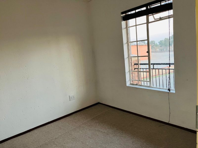 An empty bedroom featuring carpet flooring and a window with a view of the exterior.