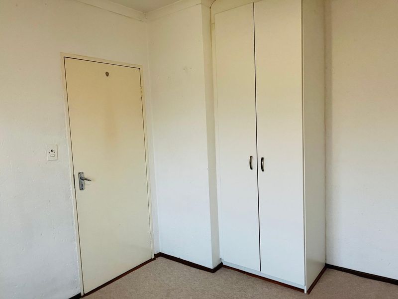 A simple, empty bedroom featuring a built-in wardrobe and neutral carpeting, offering a blank canvas for personalization.