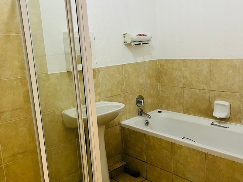 A functional bathroom featuring a pedestal basin, a bathtub with chrome fixtures, and a separate shower enclosure with tiled finishes throughout.