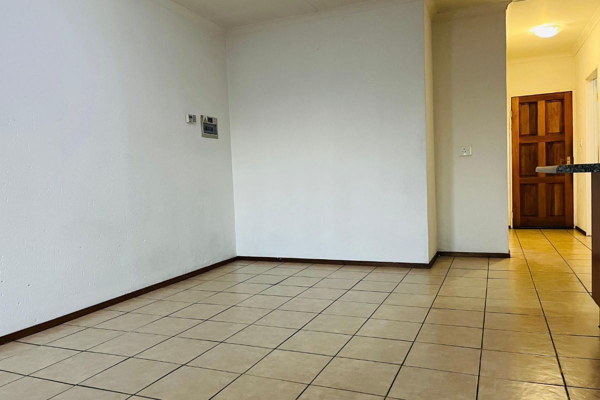 An empty living area featuring neutral tiled flooring, coved ceilings, and a solid timber door leading to an adjacent space.