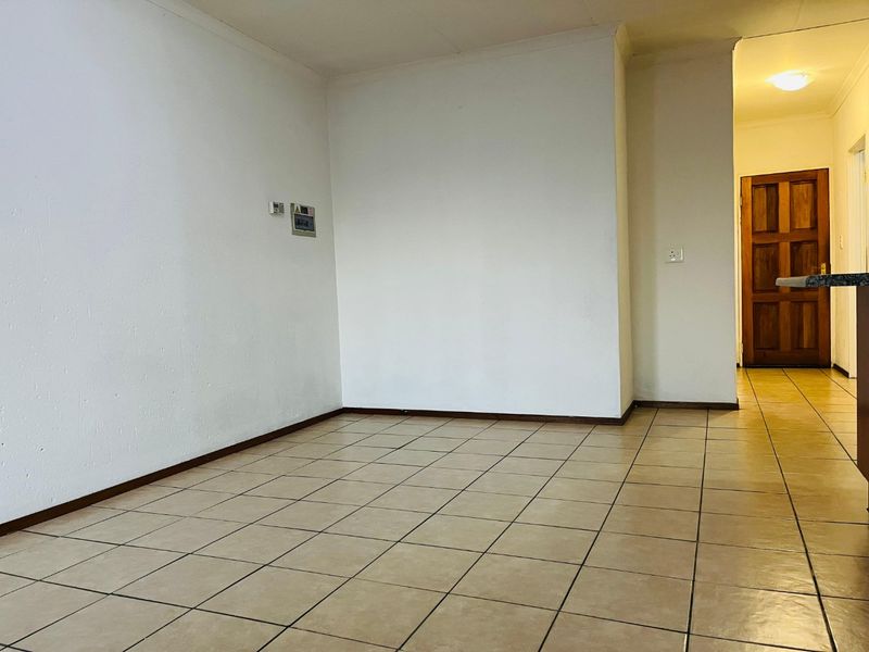 An empty living area featuring neutral tiled flooring, coved ceilings, and a solid timber door leading to an adjacent space.