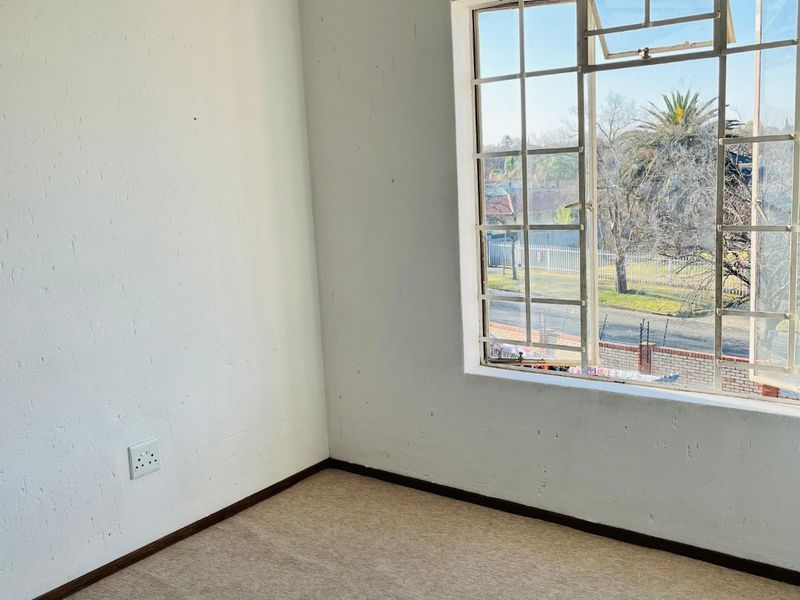 An empty bedroom featuring a grid-pattern steel window, neutral carpeting, and plain white walls, offering a blank canvas for interior design.