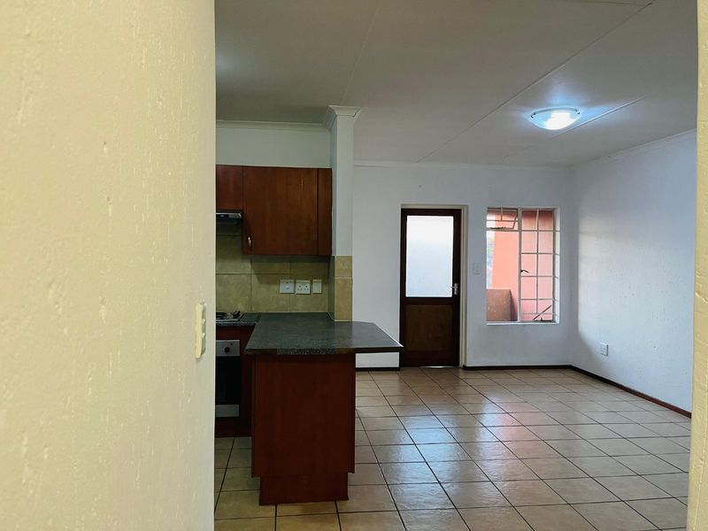 An open-plan living and kitchen area featuring tiled flooring, built-in cabinetry with a breakfast counter, and direct access to an exterior space.