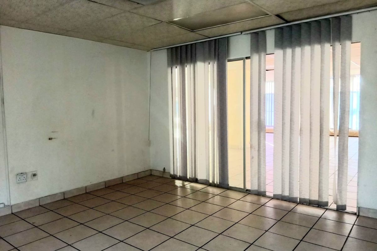 An empty commercial office space featuring ceramic tiled flooring, a suspended ceiling, and sliding glass doors with vertical blinds.