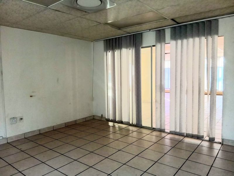 An empty commercial office space featuring ceramic tiled flooring, a suspended ceiling, and sliding glass doors with vertical blinds.