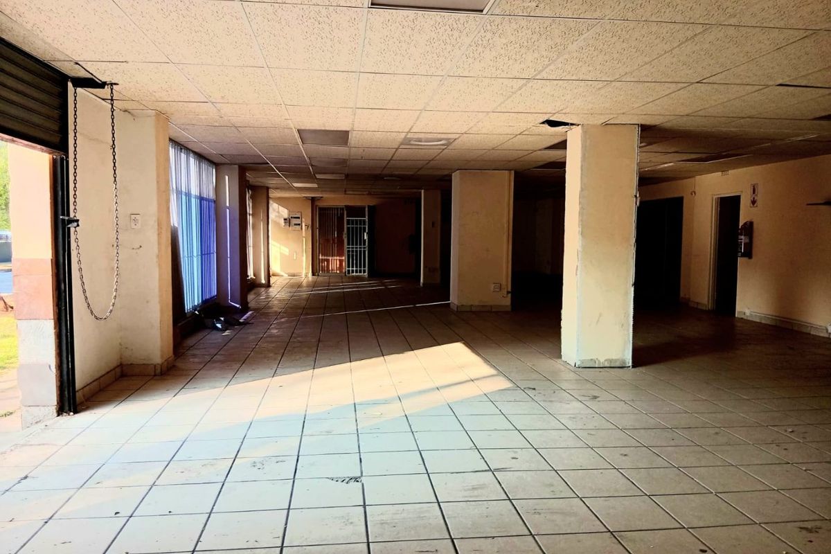 A vacant open-plan commercial space featuring ceramic tiled flooring, structural columns, and a suspended ceiling, suitable for retail or office use.