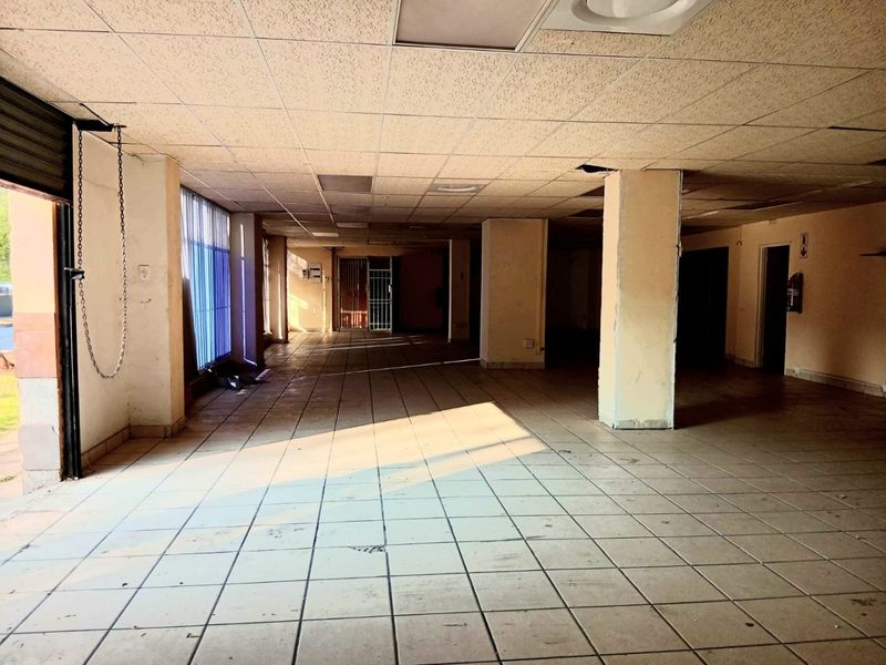 A vacant open-plan commercial space featuring ceramic tiled flooring, structural columns, and a suspended ceiling, suitable for retail or office use.