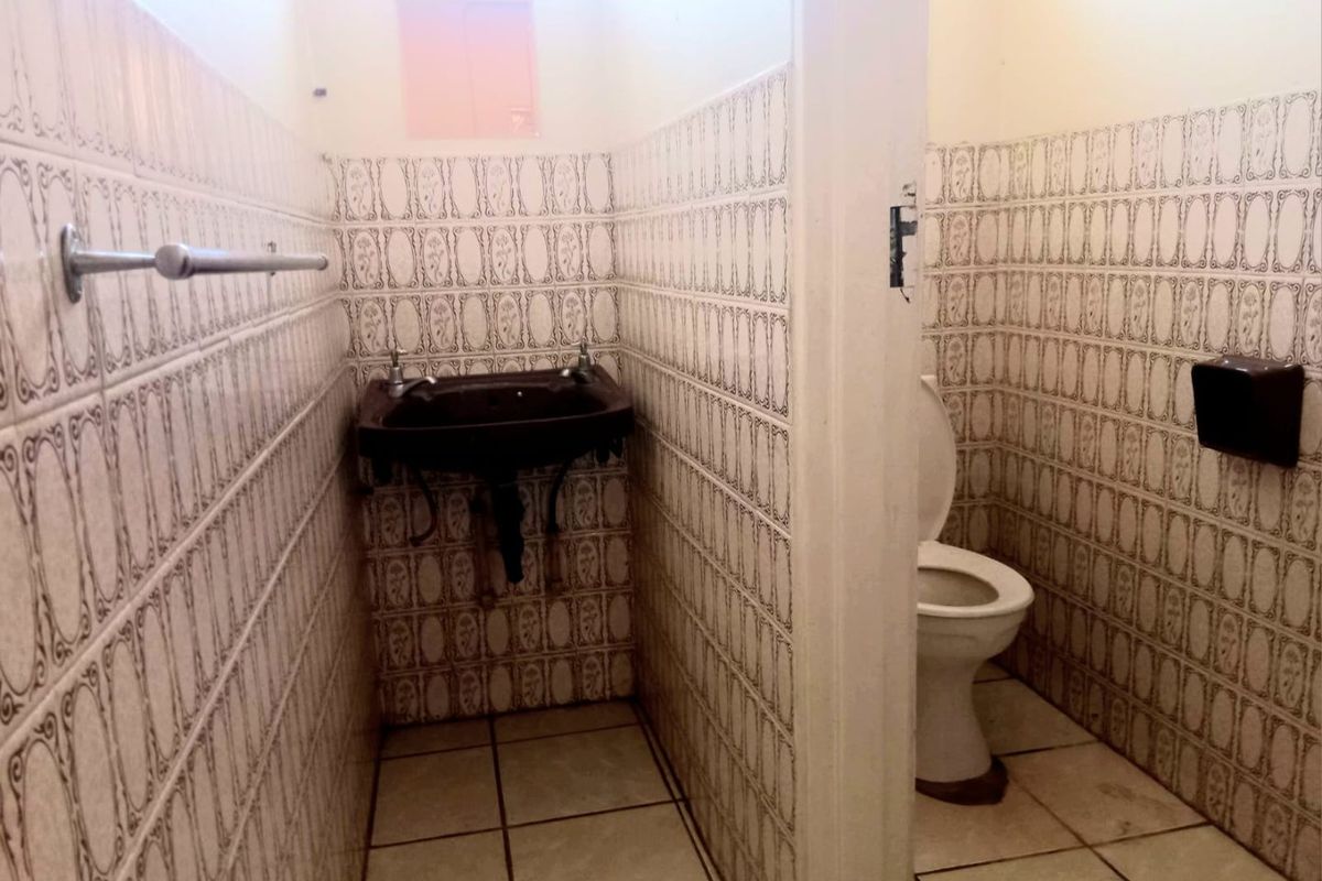 A functional commercial bathroom featuring a wall-mounted basin, toilet, and full-height decorative ceramic wall tiling.