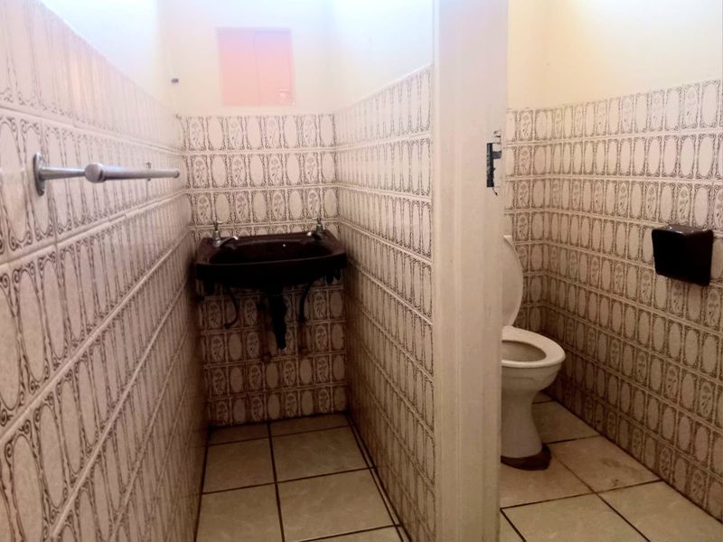 A functional commercial bathroom featuring a wall-mounted basin, toilet, and full-height decorative ceramic wall tiling.