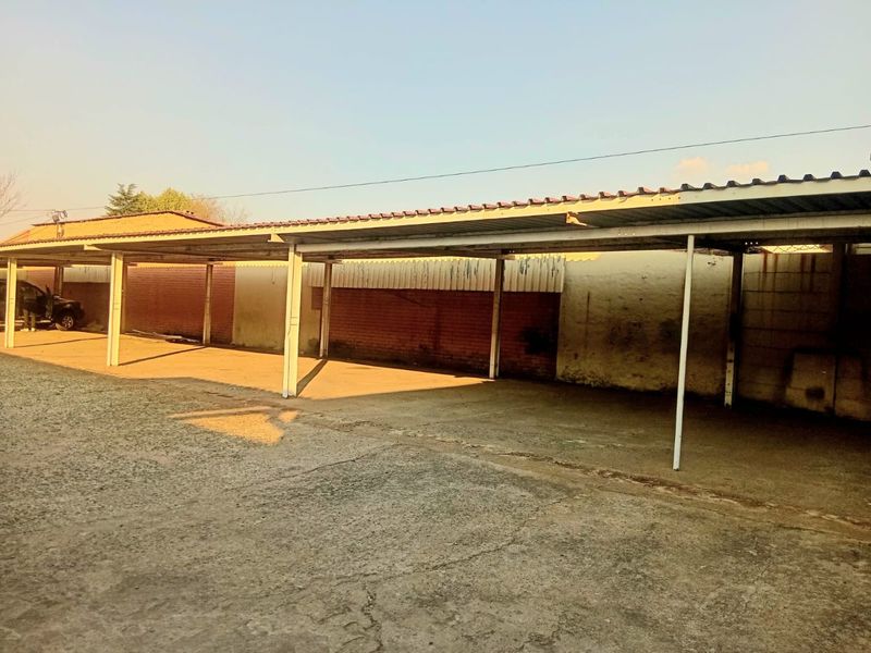 An open-air commercial carport structure featuring a metal roof, concrete flooring, and brick boundary walls, providing covered parking space.