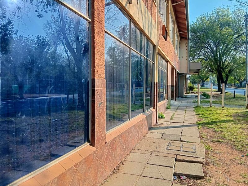 Street-level view of a commercial property featuring large glass display windows, brick facade, and a paved sidewalk area.