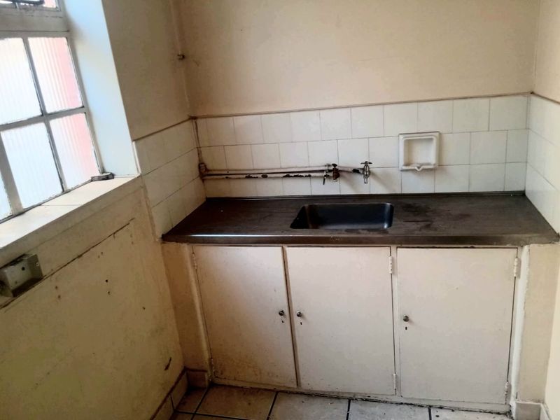 A small, dated scullery or utility area featuring a stainless steel sink, built-in cabinetry, and tiled splashback, requiring cosmetic refurbishment.