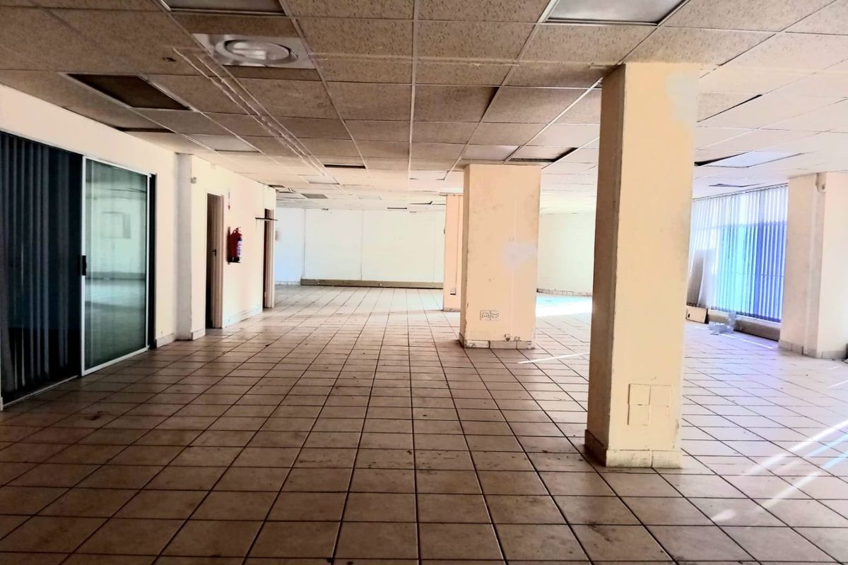 Spacious open-plan commercial office area featuring ceramic tiled flooring, structural columns, and a suspended ceiling, currently vacant and ready for renovation.