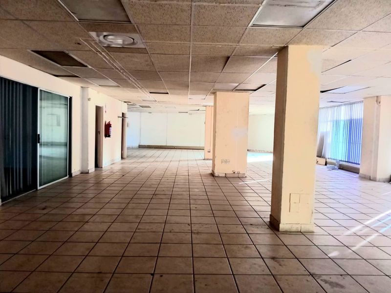 Spacious open-plan commercial office area featuring ceramic tiled flooring, structural columns, and a suspended ceiling, currently vacant and ready for renovation.