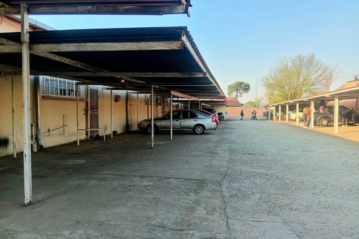 Commercial property exterior featuring a long covered parking area with concrete paving and metal roofing structures.