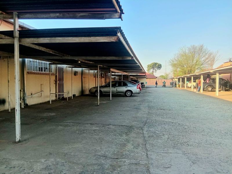 Commercial property exterior featuring a long covered parking area with concrete paving and metal roofing structures.