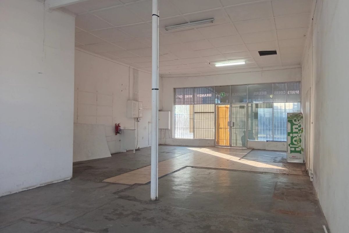 An empty commercial open-plan retail space featuring a glass storefront, concrete flooring, and a suspended ceiling, suitable for various business applications.