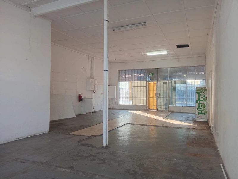 An empty commercial open-plan retail space featuring a glass storefront, concrete flooring, and a suspended ceiling, suitable for various business applications.
