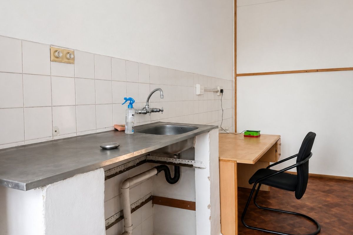 A functional utility space featuring a stainless steel sink with tiled splashback and parquet flooring, currently requiring cosmetic updates and cabinetry repairs.