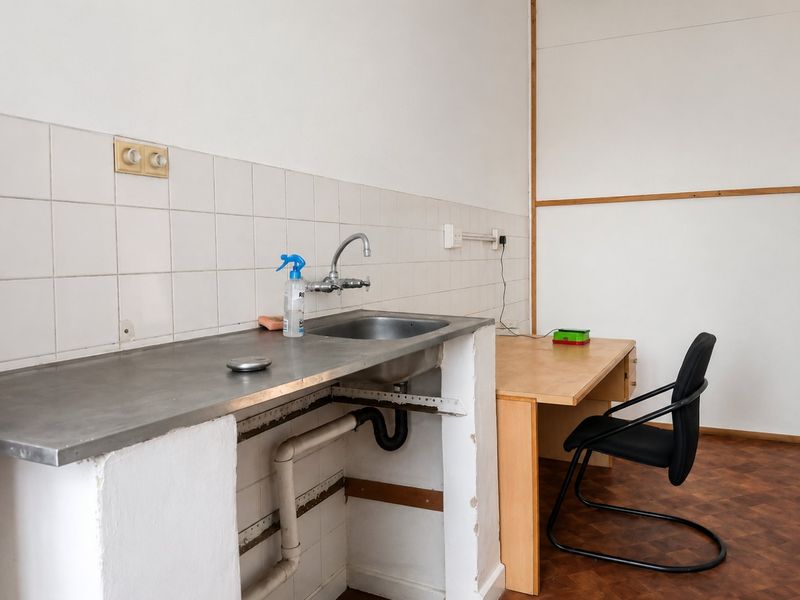 A functional utility space featuring a stainless steel sink with tiled splashback and parquet flooring, currently requiring cosmetic updates and cabinetry repairs.