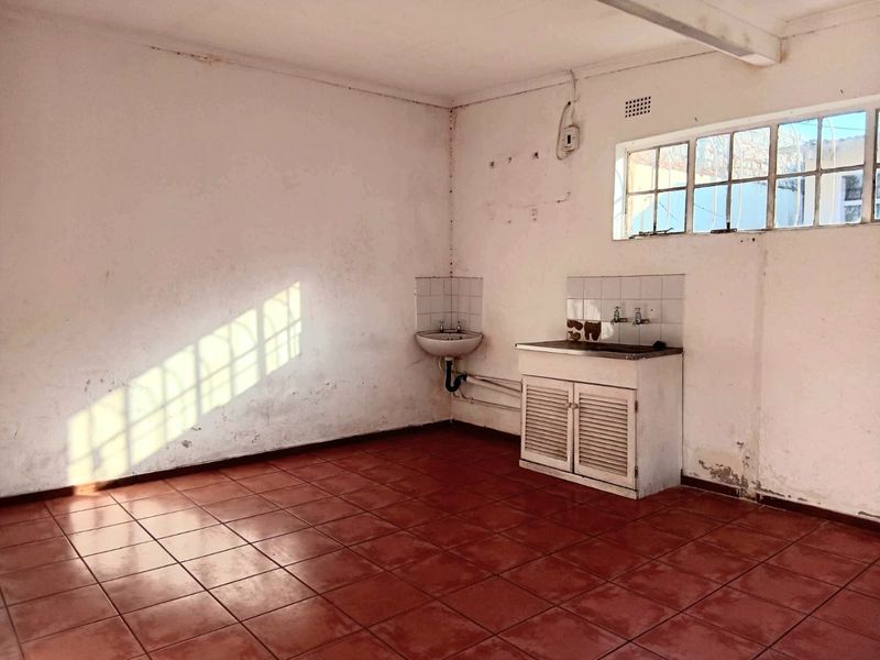 An empty, dated kitchen area featuring tiled flooring, a built-in sink unit, and a wall-mounted basin, requiring cosmetic renovation and surface repairs.