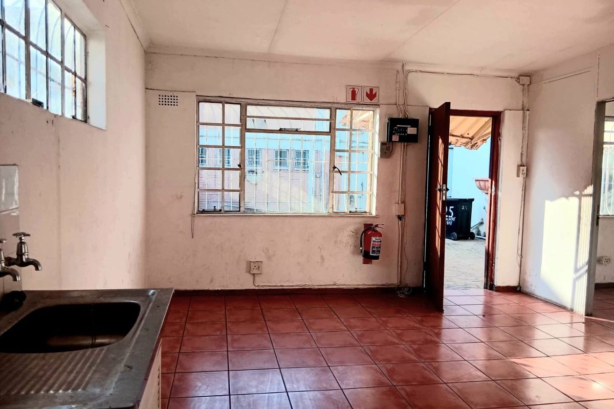 A functional, empty commercial kitchen space featuring tiled flooring, a stainless steel sink, and direct access to an outdoor area.