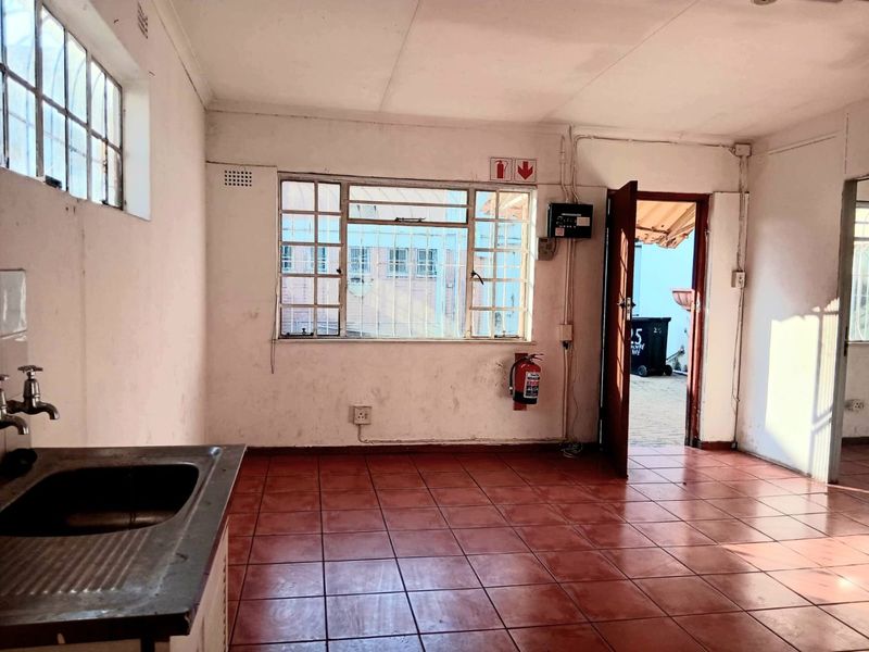 A functional, empty commercial kitchen space featuring tiled flooring, a stainless steel sink, and direct access to an outdoor area.