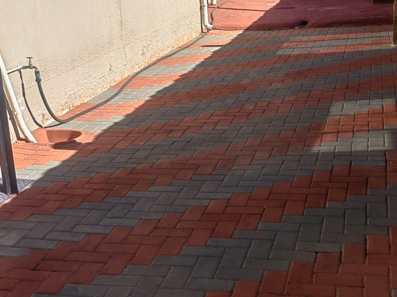 A paved rear exterior area featuring a herringbone pattern, external water tap, and security bars on the windows.