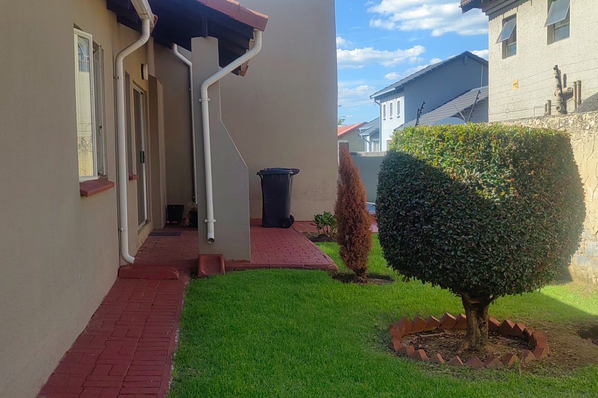 A rear exterior view of the property featuring a paved walkway, small lawn area, and boundary wall.