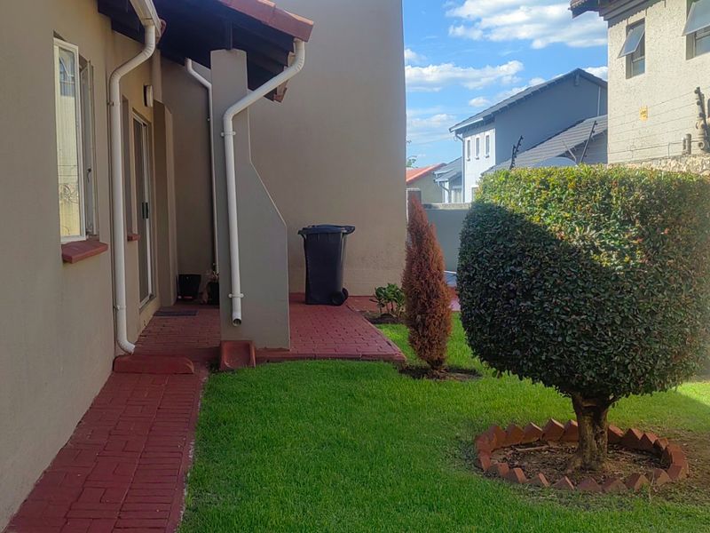 A rear exterior view of the property featuring a paved walkway, small lawn area, and boundary wall.