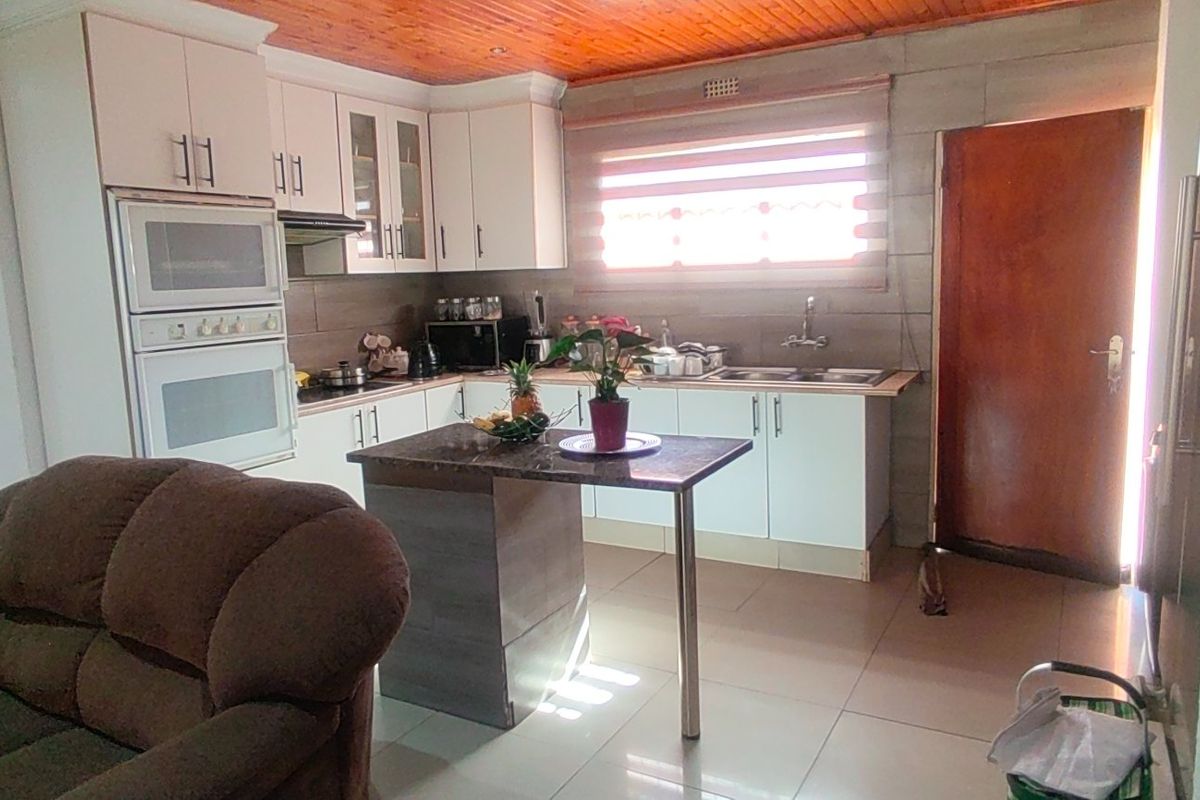A functional kitchen featuring white cabinetry, a double wall oven, a central island, and a distinctive timber-paneled ceiling with tiled flooring throughout.