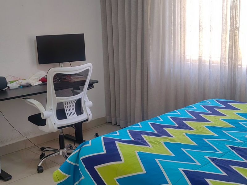A functional bedroom featuring tiled flooring, large windows with security bars, and neutral wall finishes, suitable for a comfortable sleeping or study space.