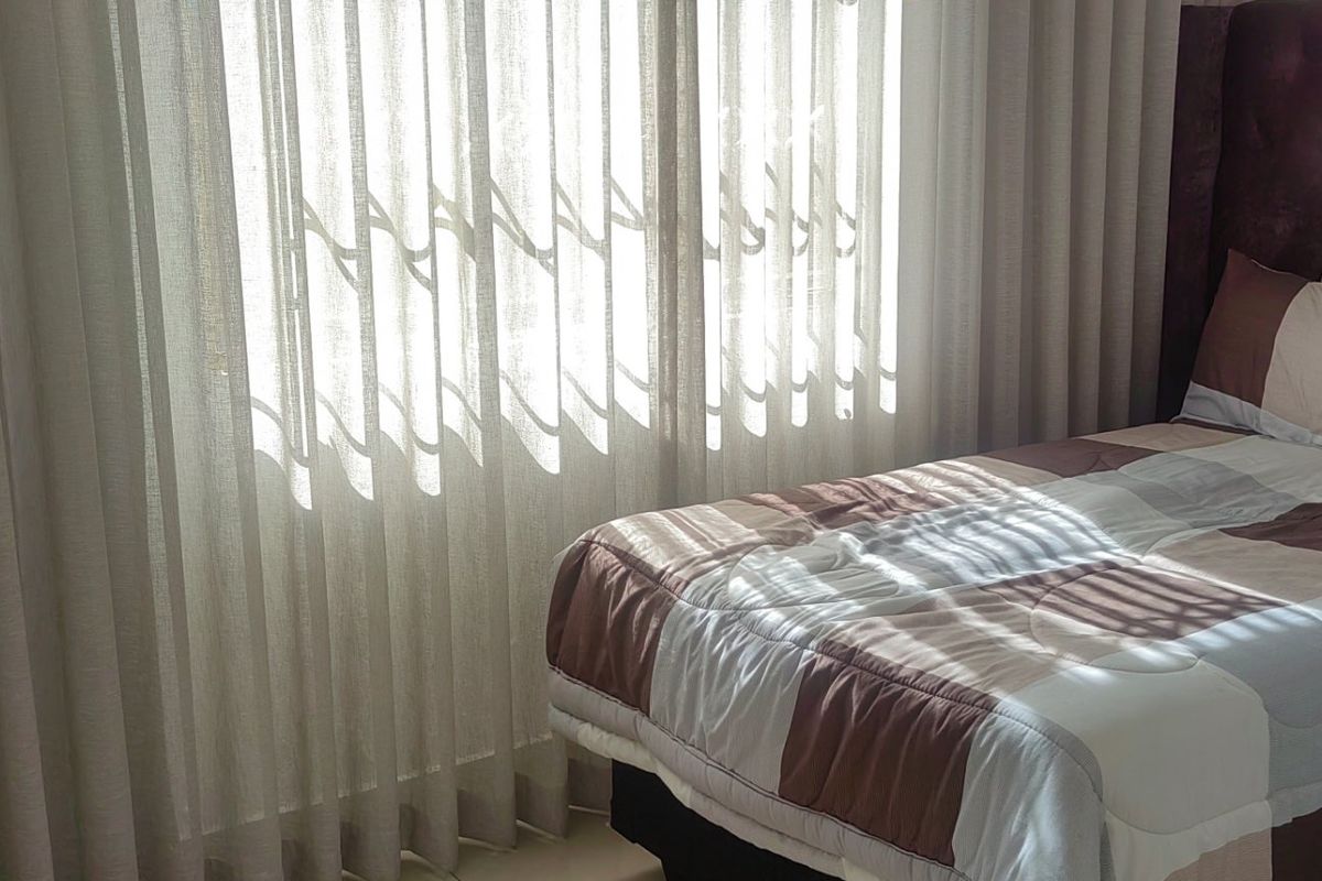 A bedroom featuring natural light filtered through floor-to-ceiling sheer curtains.