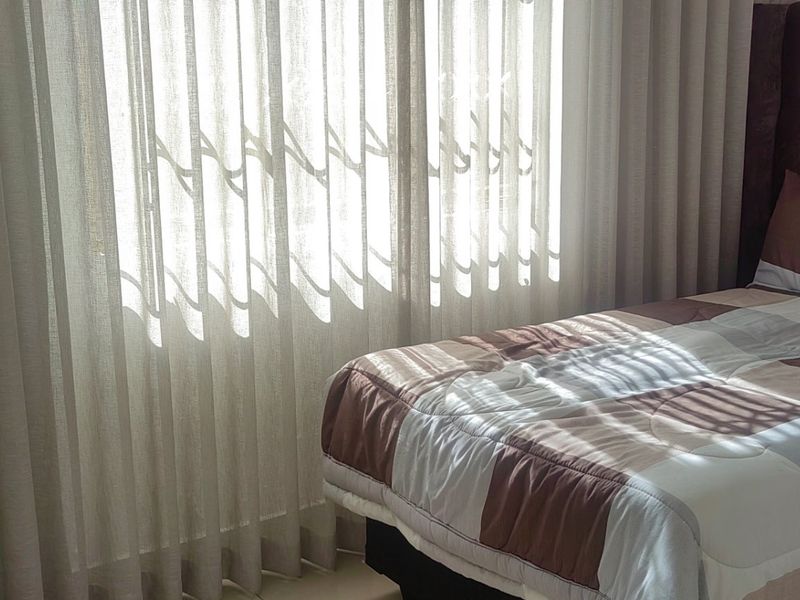 A bedroom featuring natural light filtered through floor-to-ceiling sheer curtains.