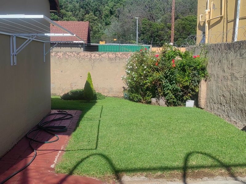 A private rear garden area featuring a well-maintained lawn, paved walkway, wall-mounted clothesline, and secure boundary walling.