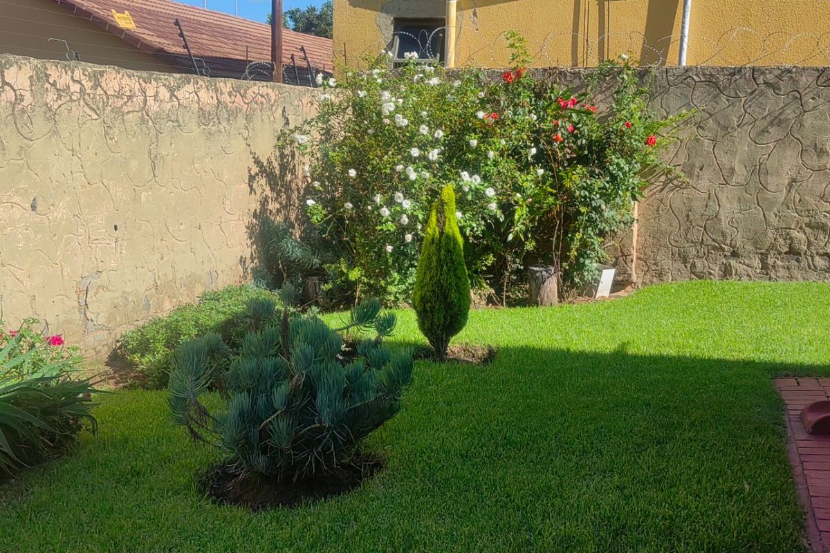 A private rear garden featuring a well-maintained lawn, established shrubs, and a secure boundary wall topped with razor wire.