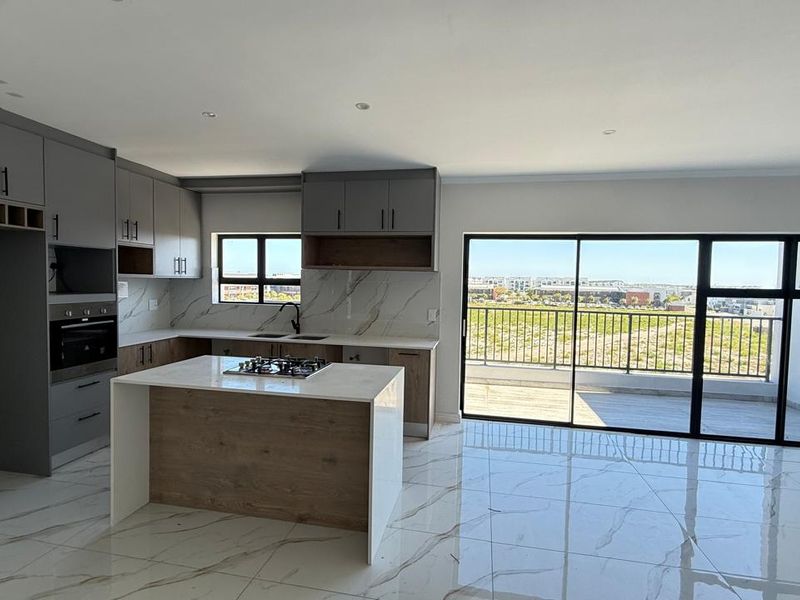 Modern open-plan kitchen and living area featuring a central island, stone countertops, high-end finishes, and large sliding doors leading to a private balcony.