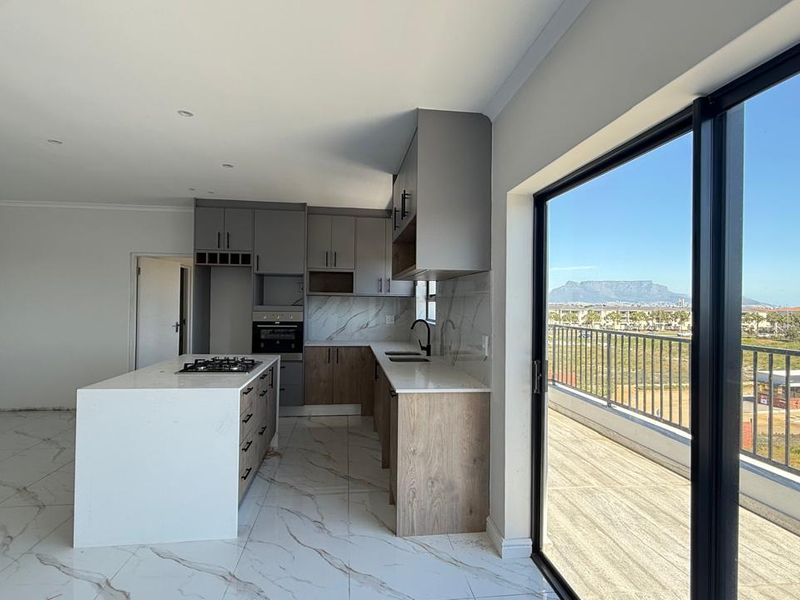 Modern open-plan kitchen featuring a central island, stone countertops, and sleek cabinetry, seamlessly flowing to a balcony with scenic mountain views.