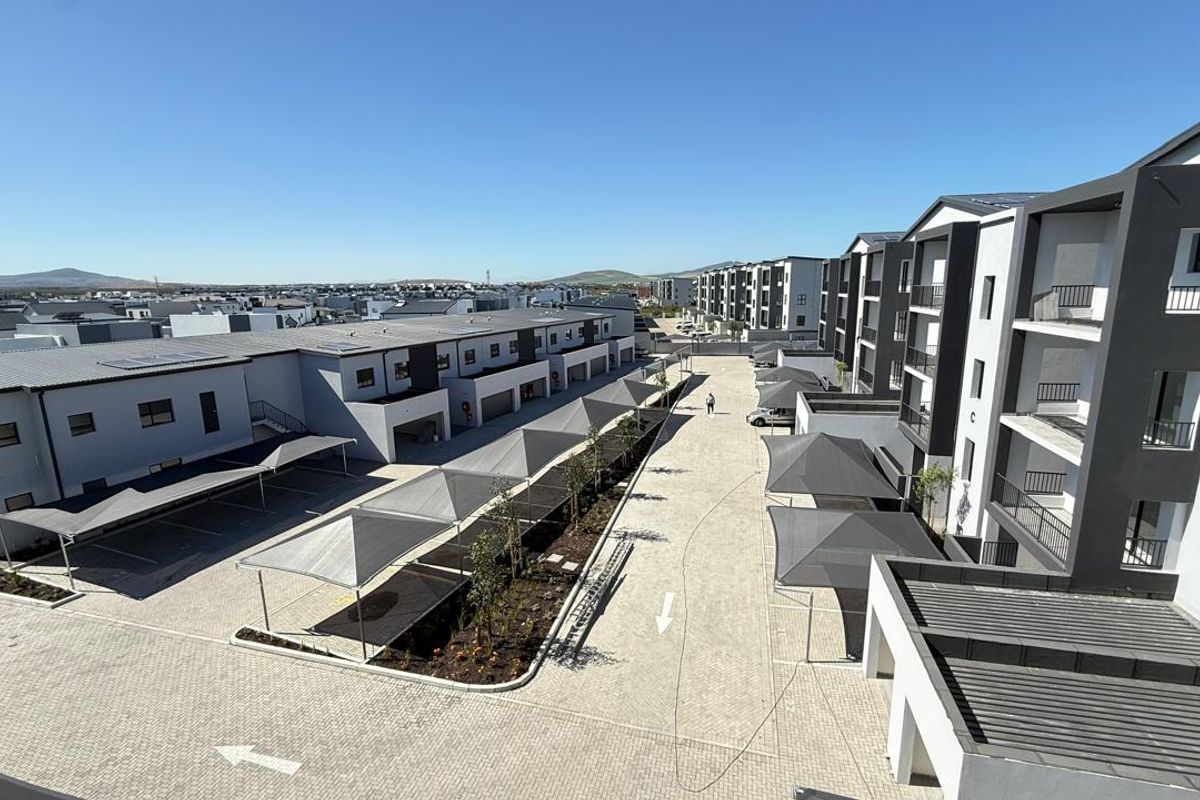 Aerial view of a modern apartment complex featuring paved driveways, shade cloth parking bays, and multi-story residential buildings.